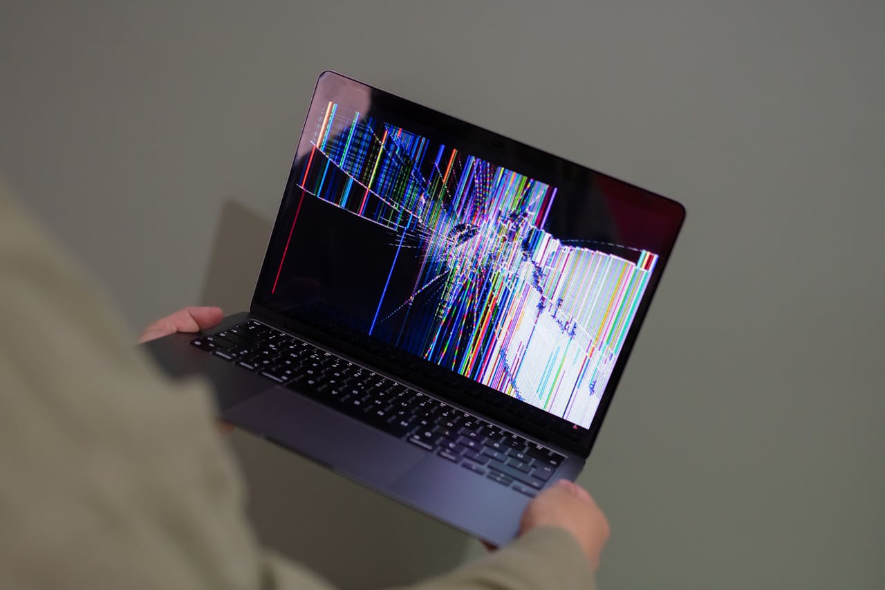 services-04 A broken laptop screen displayed with colorful glitch being held by a person.